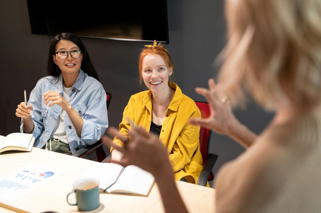 Happy young intercultural businesswomen in casualwear looking at business coach
